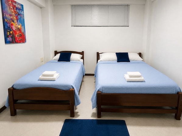 A room with two wooden beds, each with a blue bedspread and white pillows, and a blue rug on the floor.
