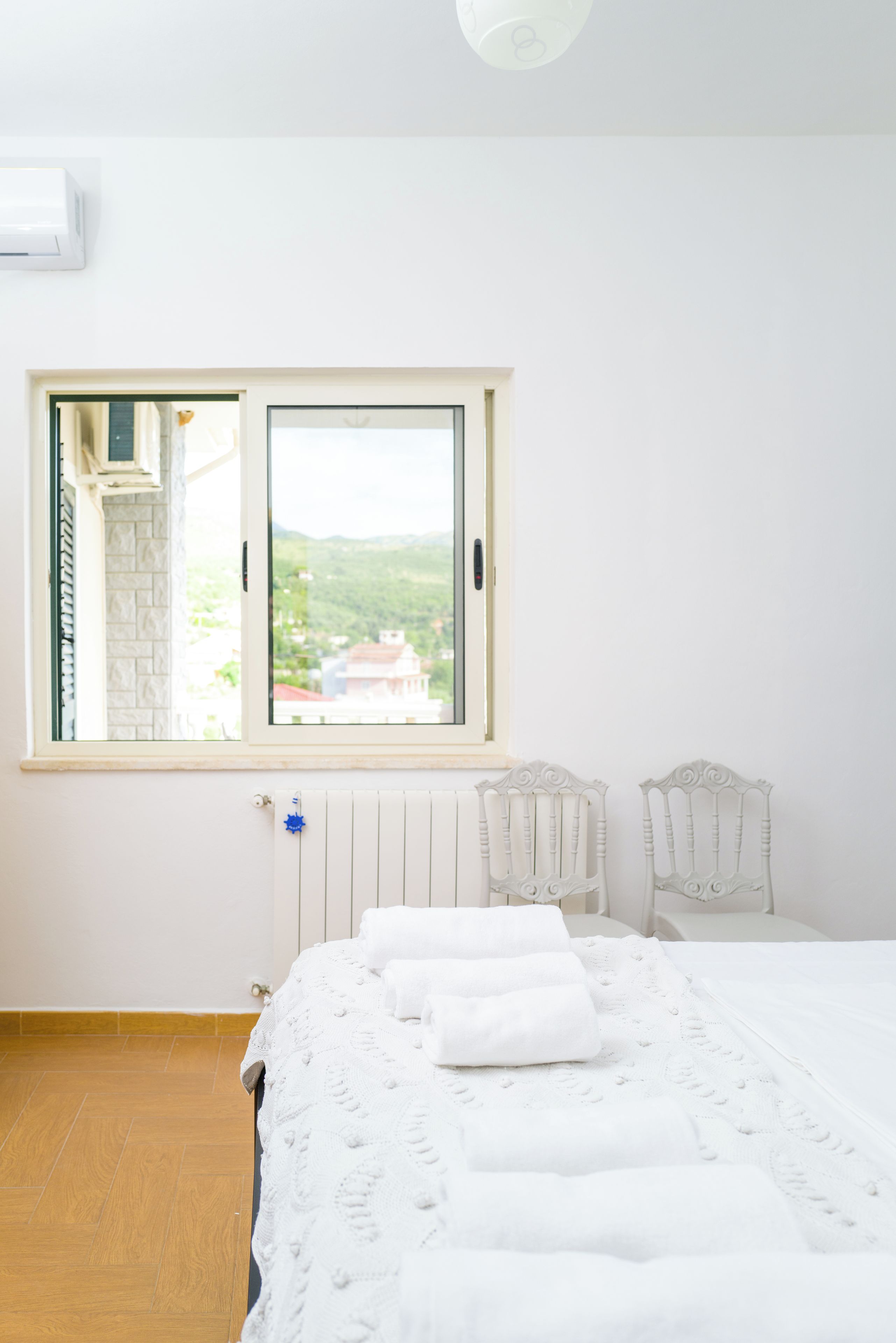 A room with a large window, a bed with white linens, two white chairs, and a radiator.