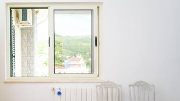 A room with a large window, a bed with white linens, two white chairs, and a radiator.