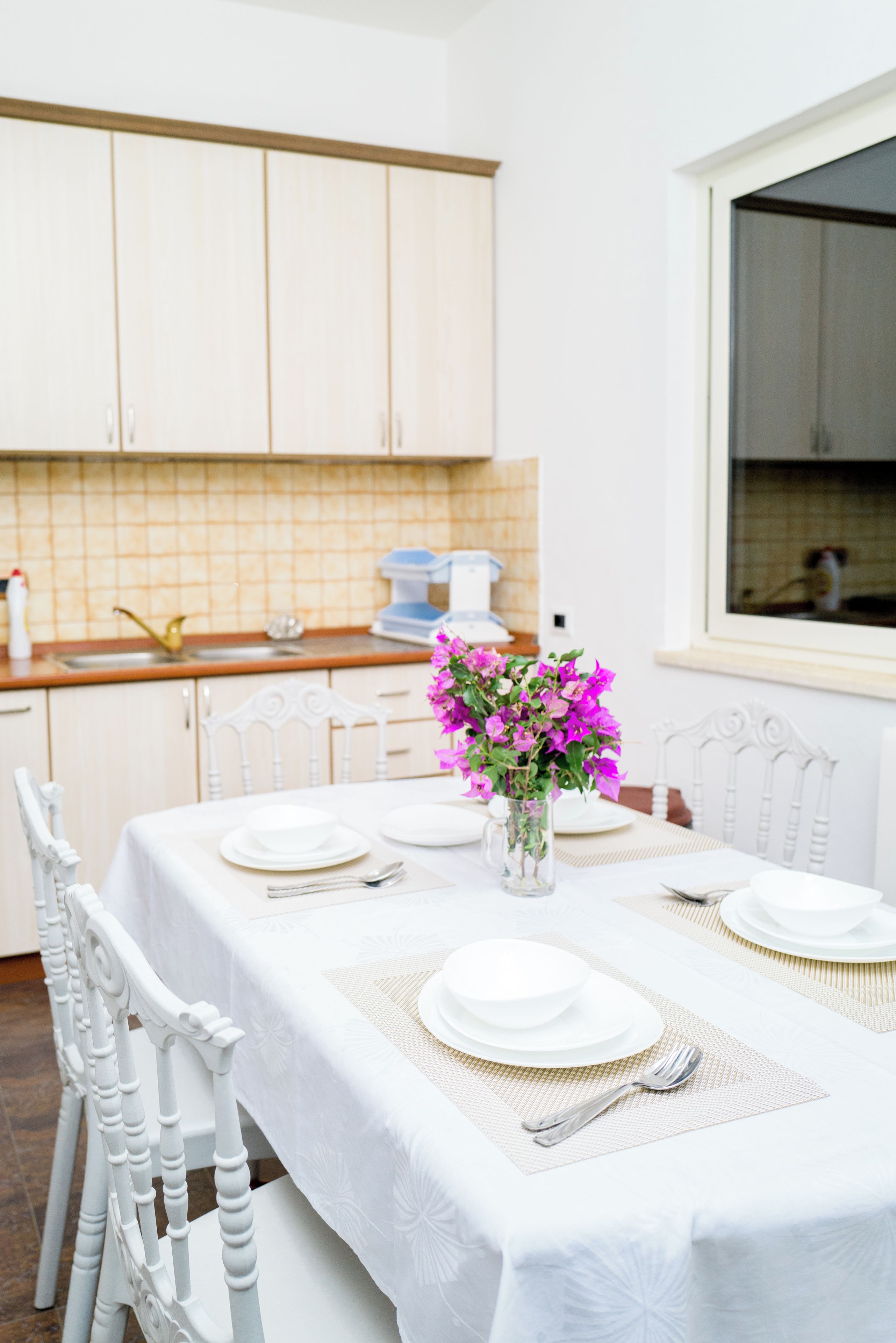 A dining area with a table set for four, white chairs, and a vase with flowers.