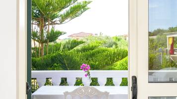 A balcony with a table and chair, overlooking a lush garden and a distant building.
