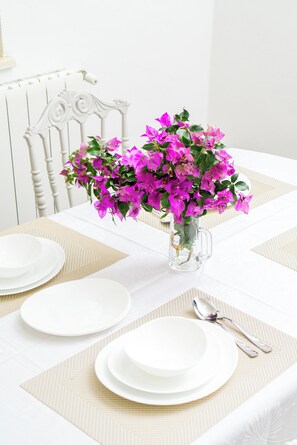 Une table dressée avec des assiettes blanches, un verre transparent et un vase rempli de fleurs roses.