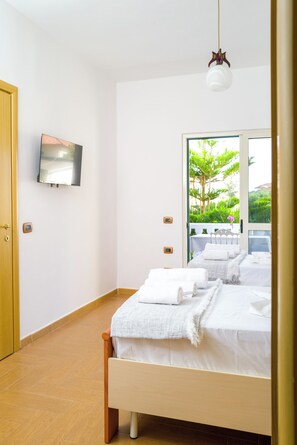 A modern bedroom with a bed, a television mounted on the wall, and a view of greenery outside.