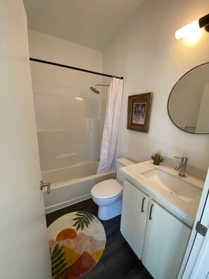 Et badeværelse med bruser, toilet, vask og spejl.