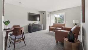 A living room with a sofa, a television, a dining table with chairs, and a decorative vase. - Gray's Lake - 2BR 1BA, Washer, Parking - Near CBD Downtown (Des Moines)