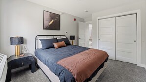 A bedroom with a bed, bedside tables, a lamp, a painting, and a wardrobe. - Gray's Lake - 2BR 1BA, Washer, Parking - Near CBD Downtown (Des Moines)