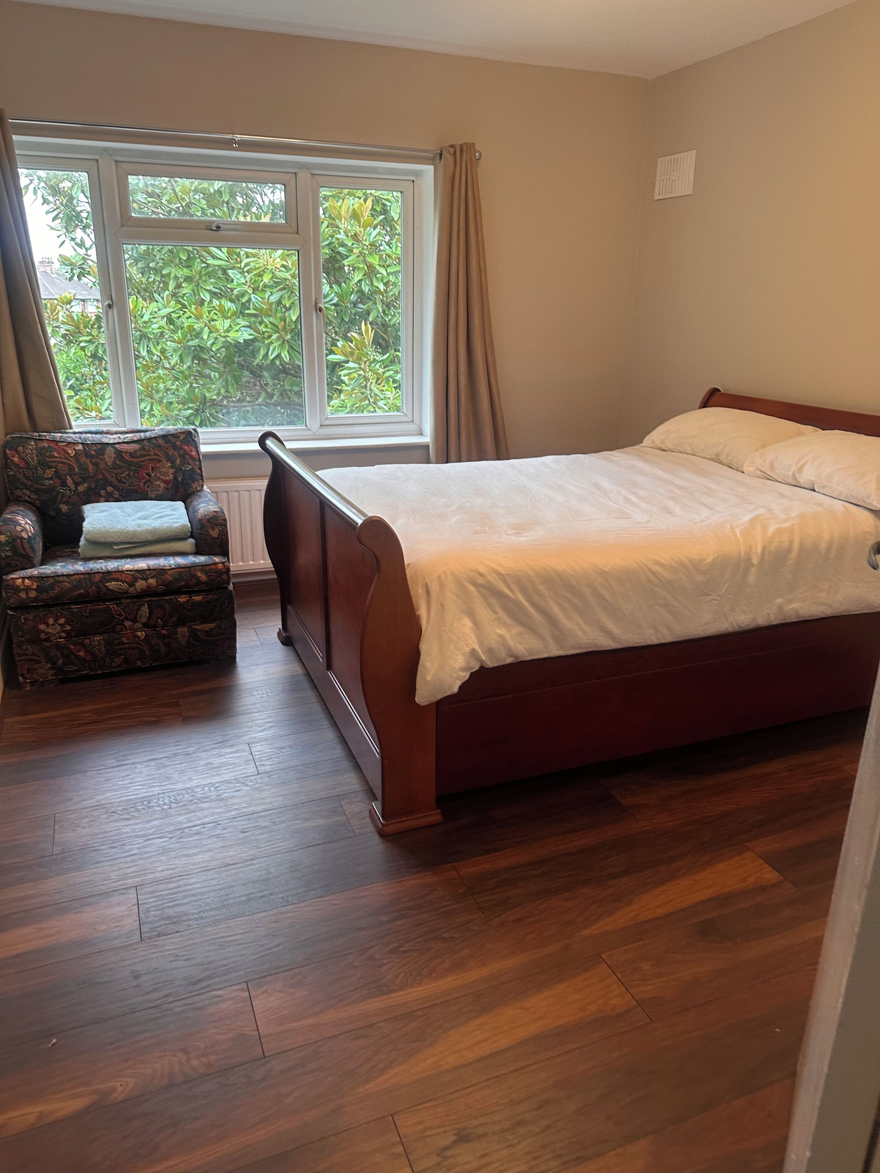 Een slaapkamer met een bed, een stoel, een raam met gordijnen en een radiator.