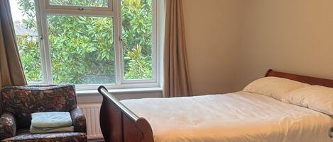 Un dormitorio con cama, una silla, un ventanal con cortinas y un radiador.