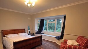 A bedroom with a large bed, a window with curtains, a sofa, and a chandelier. - Stylish 4-Bed Detached Home Close to Grantham Town & Amenities (Grantham)