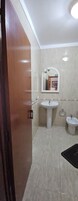 Un baño con puerta de madera, un espejo grande, dos lavamanos y un tapete negro en el suelo.