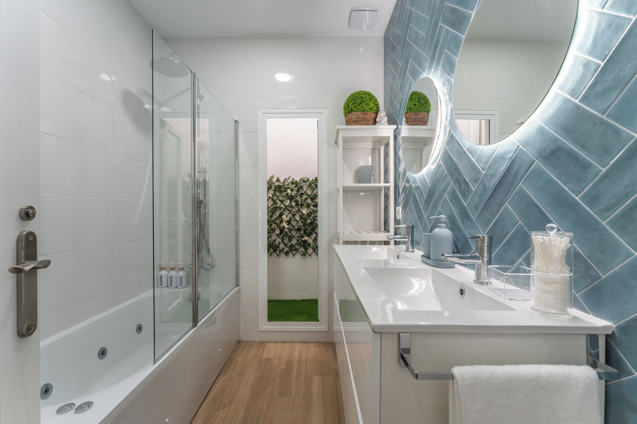 Een moderne badkamer met een douchecabine van glas, witte tegels, een grote spiegel en een kleine groene plant.