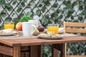 A wooden table with breakfast items including fruit, bread, and juice, set against a backdrop of greenery. - Casa Augusto - next to the Roman Theater, with a garage (Mérida)