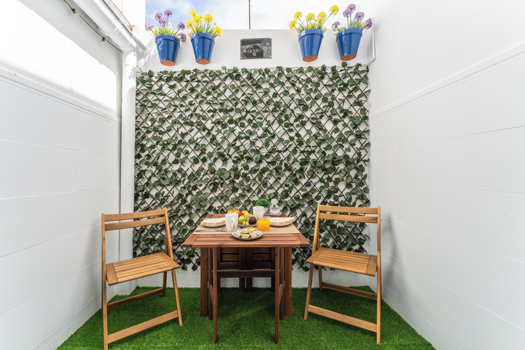 Een klein terras met een tafel en twee stoelen, een decoratieve muur met klimplanten en bloempotten.