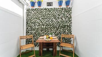 Een klein terras met een tafel en twee stoelen, een decoratieve muur met klimplanten en bloempotten.