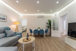 A modern living room with a sofa, a dining table with chairs, a TV, and a lamp.