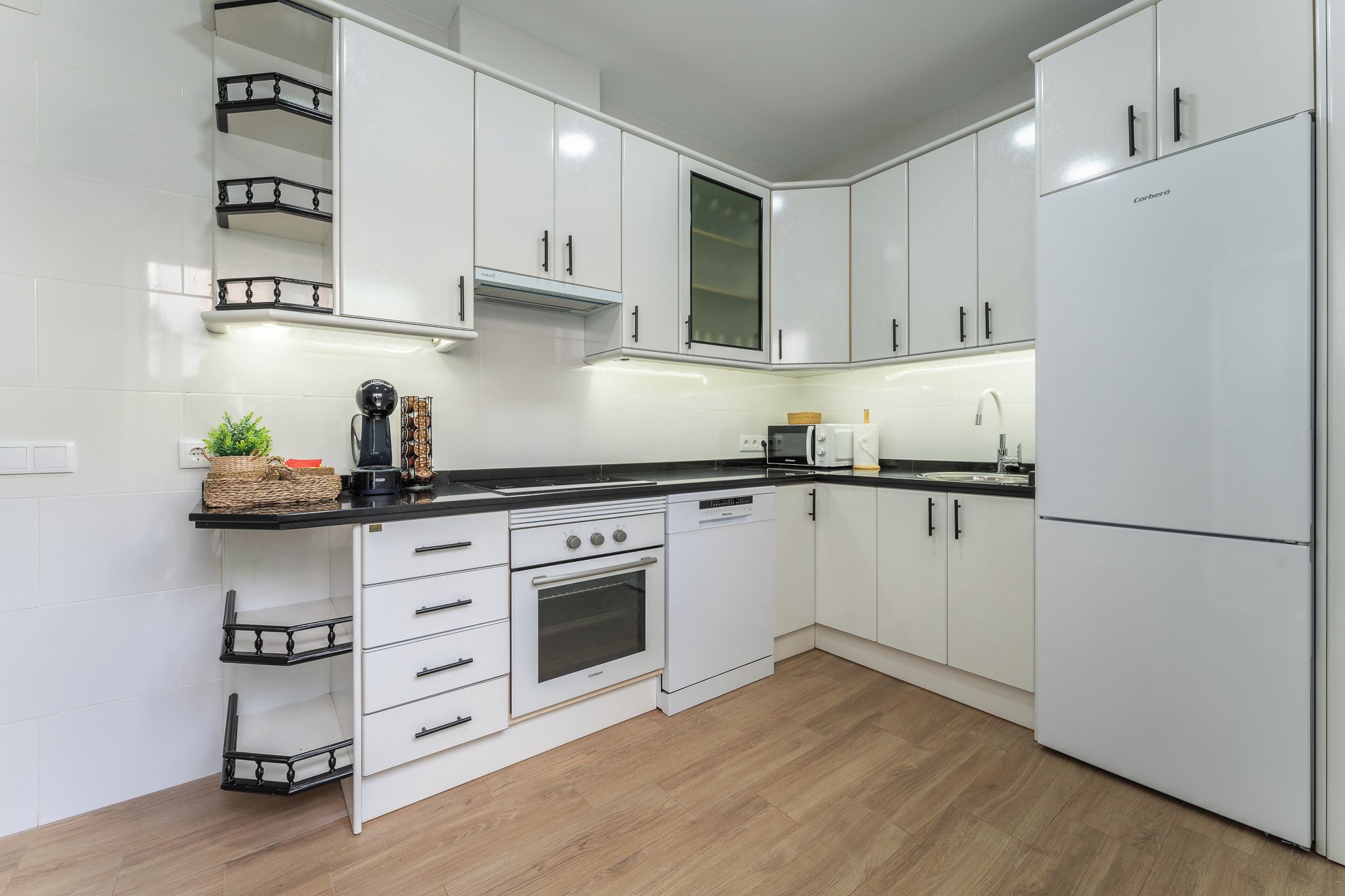 Een moderne keuken met witte kasten, een zwart aanrecht, een ingebouwde oven en een koelkast.