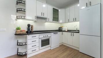Een moderne keuken met witte kasten, een zwart aanrecht, een ingebouwde oven en een koelkast.