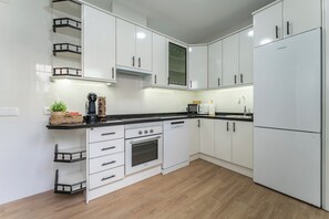 A modern kitchen with white cabinetry, a black countertop, a built-in oven, and a refrigerator.