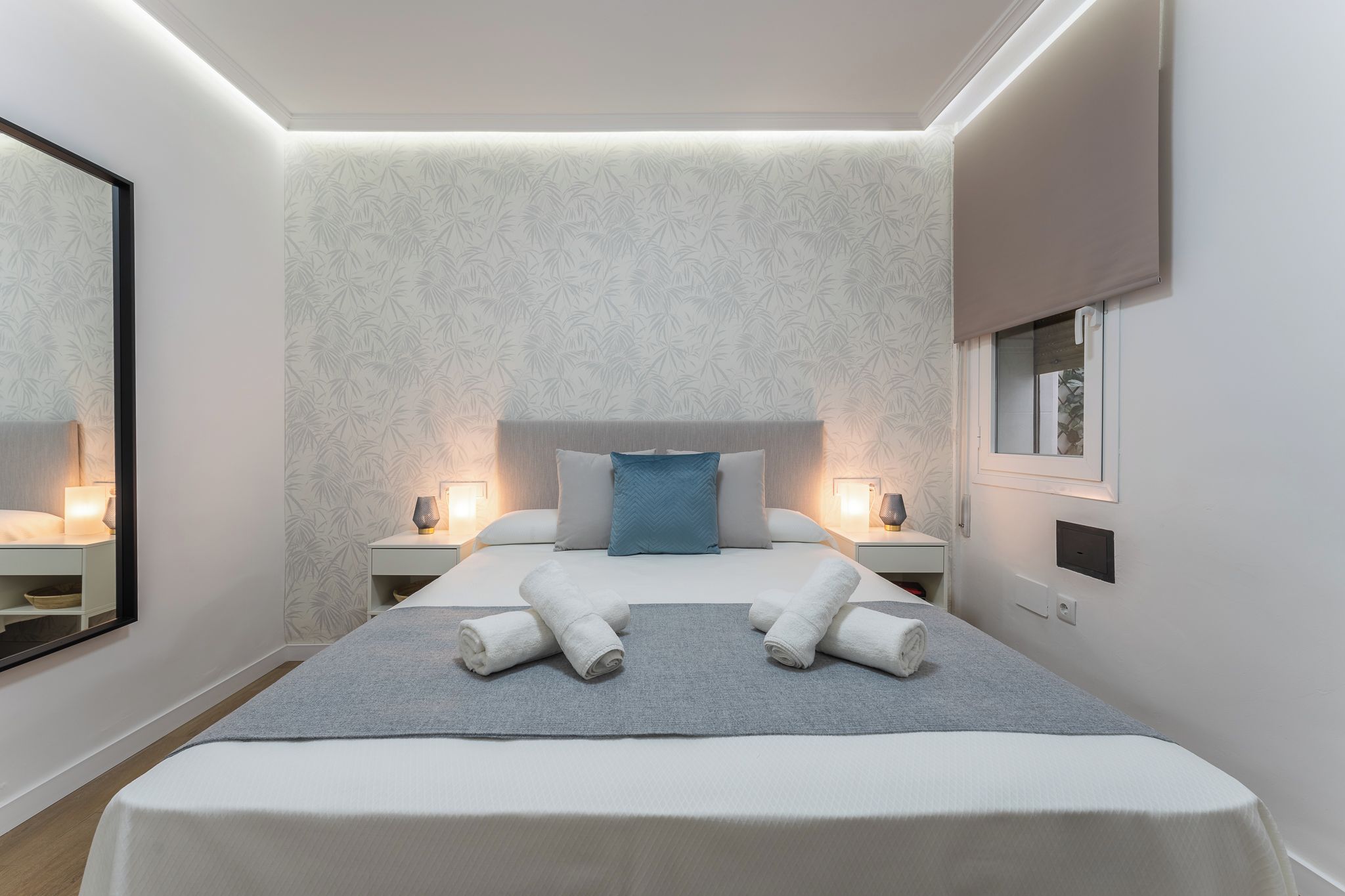 Een moderne hotelkamer met een groot bed, twee nachtkastjes, een spiegel en een raam.