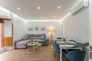 A modern living room with a grey sofa, a dining table set for four, and a standing lamp. - Casa Augusto - next to the Roman Theater, with a garage (Mérida)