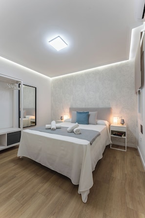 A modern bedroom with a large bed, bedside tables, a mirror, and a ceiling light. - Casa Augusto - next to the Roman Theater, with a garage (Mérida)