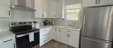 A modern kitchen with white cabinets, stainless steel appliances, and a window providing natural light.