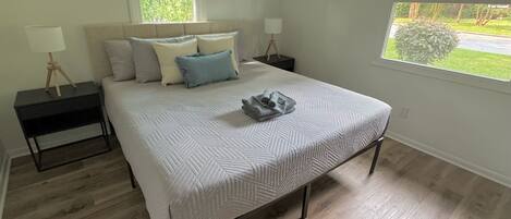 A bedroom with a bed, two nightstands, a window, and a view of greenery outside.