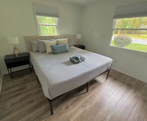 Une chambre à coucher avec un lit, deux tables de chevet, une fenêtre et une vue sur la verdure.