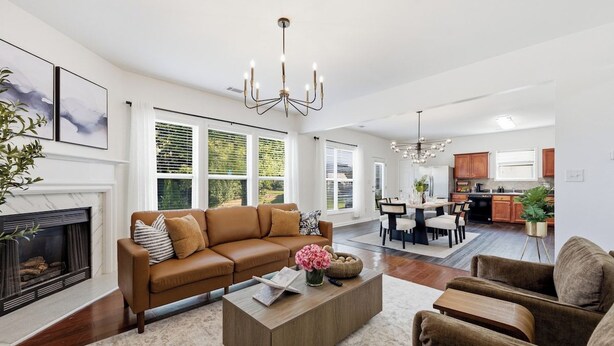 Una sala de estar moderna con chimenea, un sofá marrón, una mesa de centro y un comedor con candelabro.