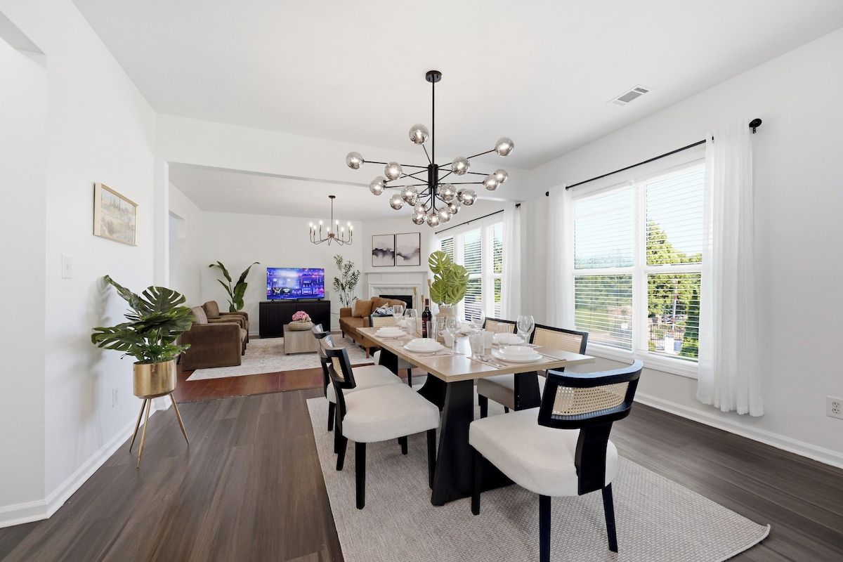 A modern dining area with a long table, chairs, and a chandelier.