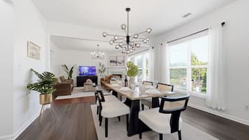 A modern dining area with a long table, chairs, and a chandelier.