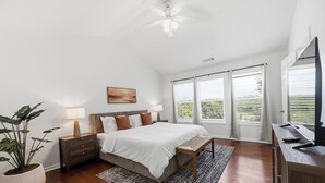 Un dormitorio con cama, mesitas de noche, escritorio, silla, ventilador de techo y ventana con persianas.