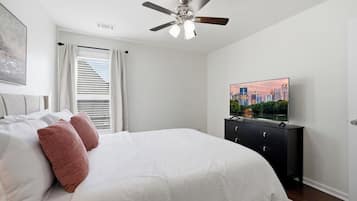 A bedroom with a bed, a ceiling fan, a TV on a dresser, and a window with curtains.