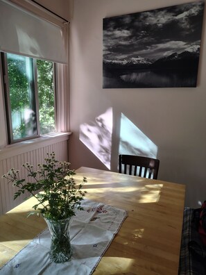 Ein Essbereich mit Tisch, Blumen in einer Vase, einem Fenster und einem Bild an der Wand.