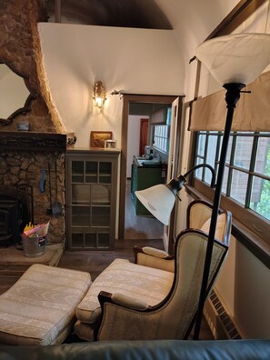 A cozy interior with a stone fireplace, a wooden cabinet, a green table, and a chair. - La Finca 1928 w stream in Valley of Moon/Historical 1 Bd 2Bath two-level cabin (Crestline)