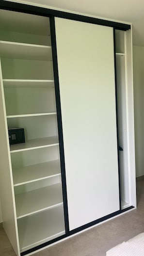A sliding closet with multiple shelves and a small safe.