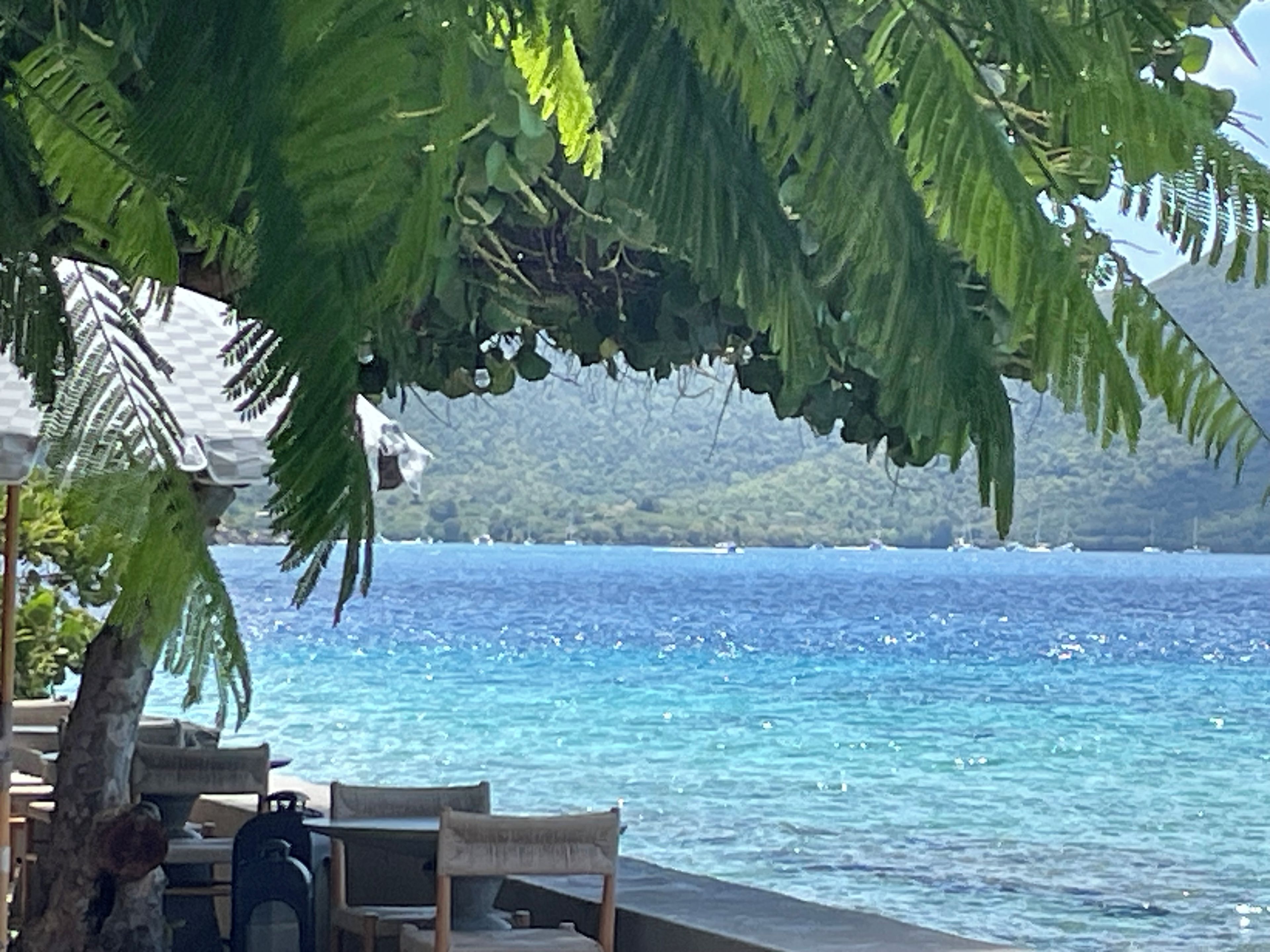 A seaside view with a table and chairs under a shaded area, overlooking the ocean.