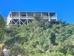 A multi-story building with a balcony on the upper level, surrounded by dense greenery. - Home on Beach on Private Island Available for Holidays Overlooking Caribbean Sea (St John)