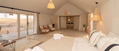 Un dormitorio amplio con una cama grande, una zona de estar con sillones y vistas a un espacio exterior por una puerta corrediza.