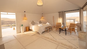 A spacious room with a large bed, two chairs, a small table, and a view of the outdoors.