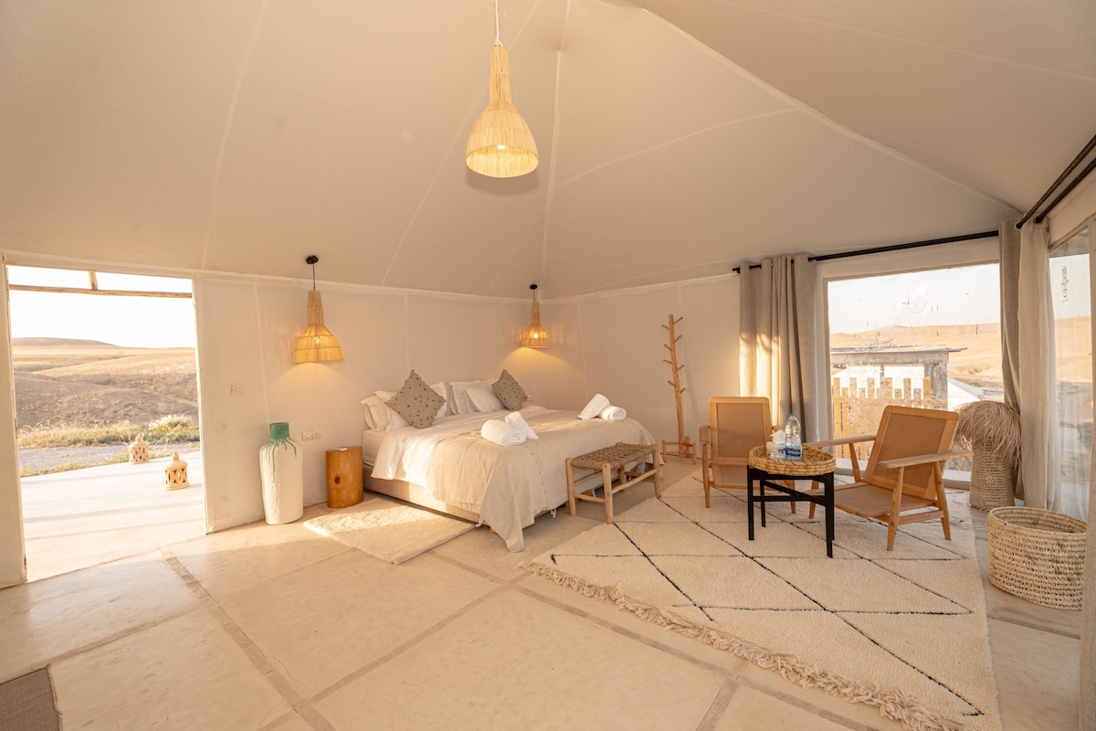 Une pièce spacieuse avec un grand lit, deux chaises, une petite table et une vue sur l’extérieur.