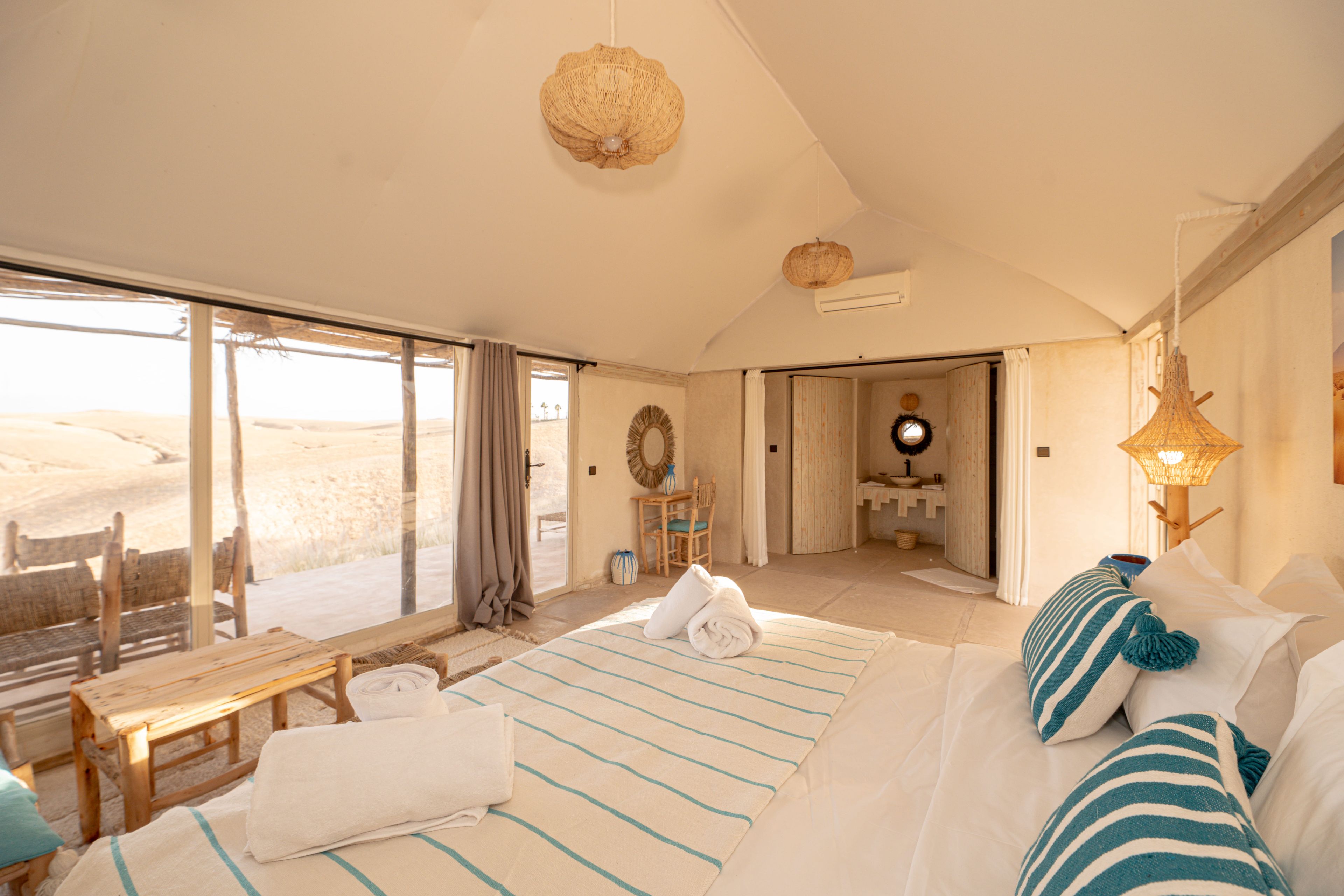 Un dormitorio amplio con una cama grande, un banco de madera y vistas al desierto a través de la ventana.