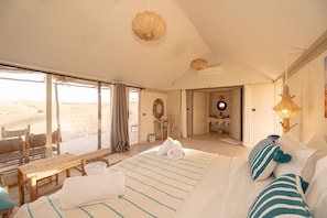 A spacious bedroom with a large bed, a wooden bench, and a view of the desert through the window.