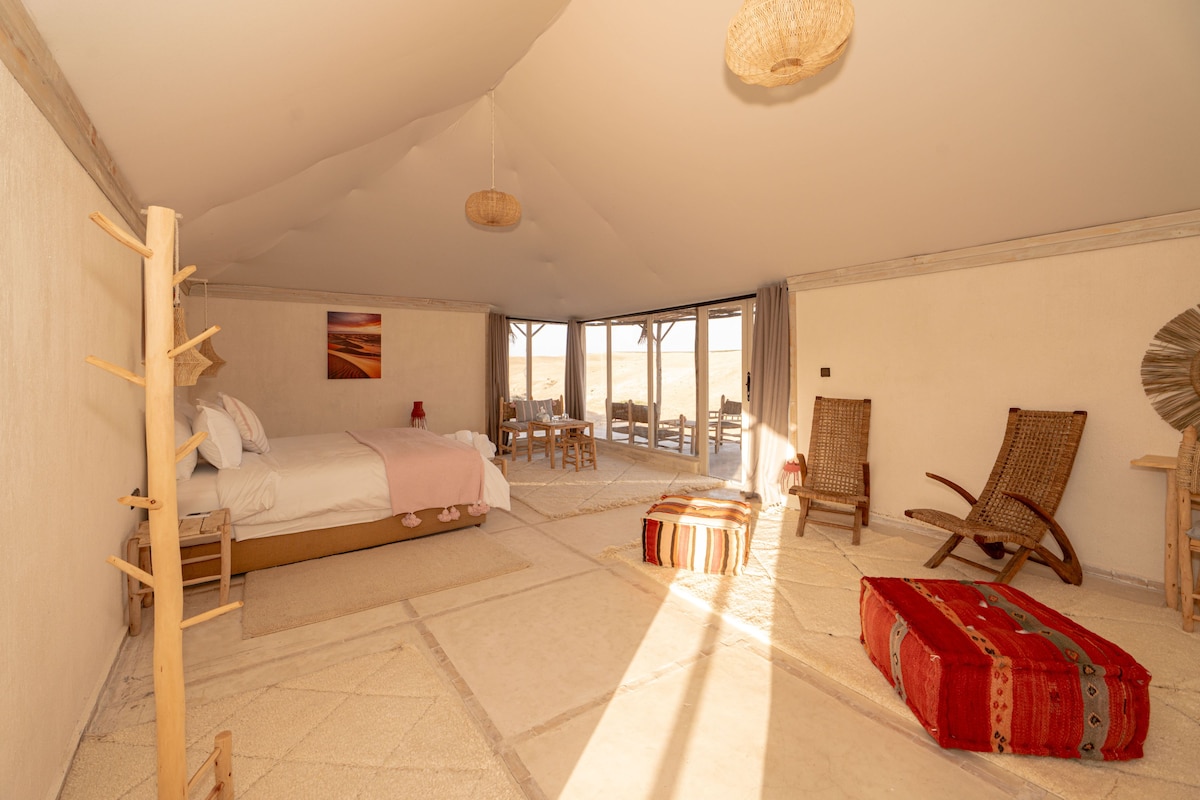 Une chambre spacieuse avec un grand lit, un coin salon comprenant un fauteuil et une table, et une vue par la fenêtre.