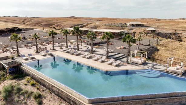 A pool area with lounge chairs and palm trees, surrounded by a desert landscape.