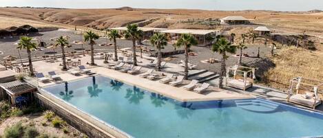 A pool area with lounge chairs and palm trees, surrounded by a desert landscape.