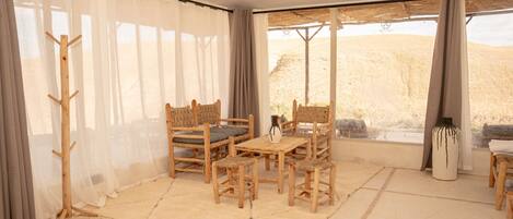 A room with a wooden table and chairs, a rug, and a view of a desert landscape through large windows.