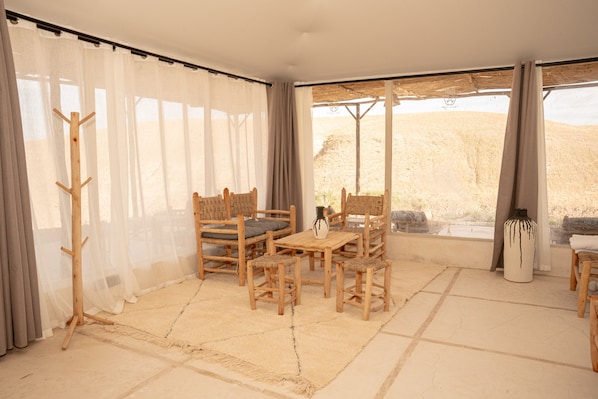 A room with a wooden table and chairs, a rug, and a view of a desert landscape through large windows.
