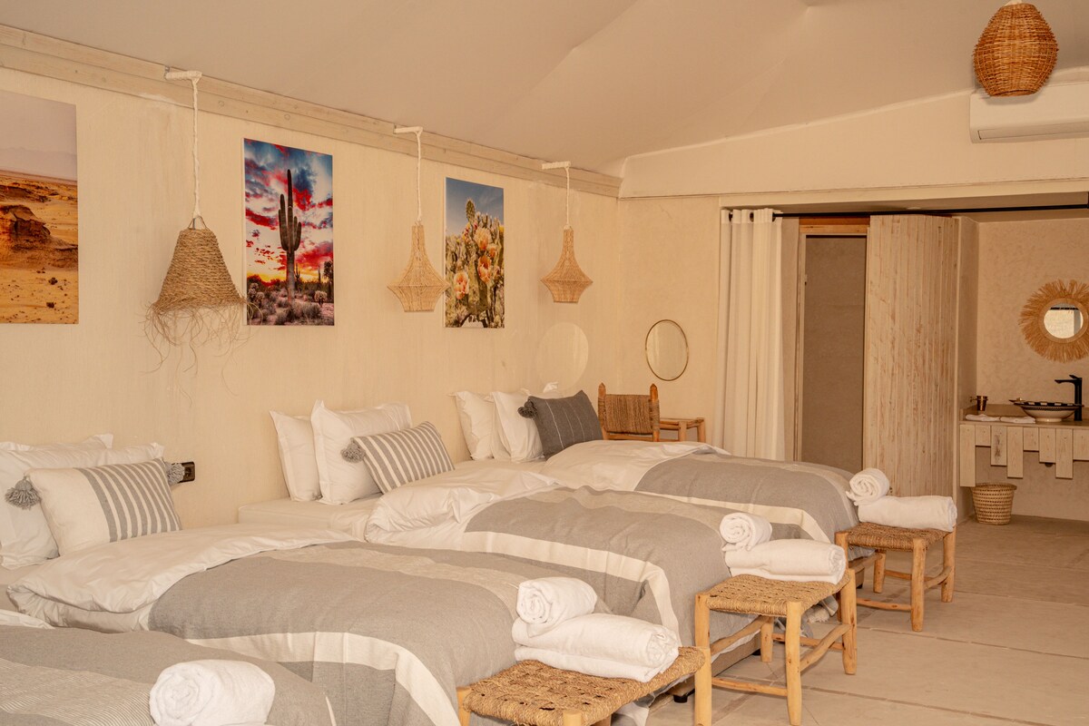 Une chambre d’hôtel avec un grand lit, deux tables de chevet, un miroir et une salle de bain équipée d’un lavabo et d’un porte-serviettes.