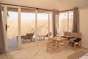 Habitación con un amplio ventanal corredera que da a vistas del desierto, amueblada con una mesa de madera, sillas y un sofá.